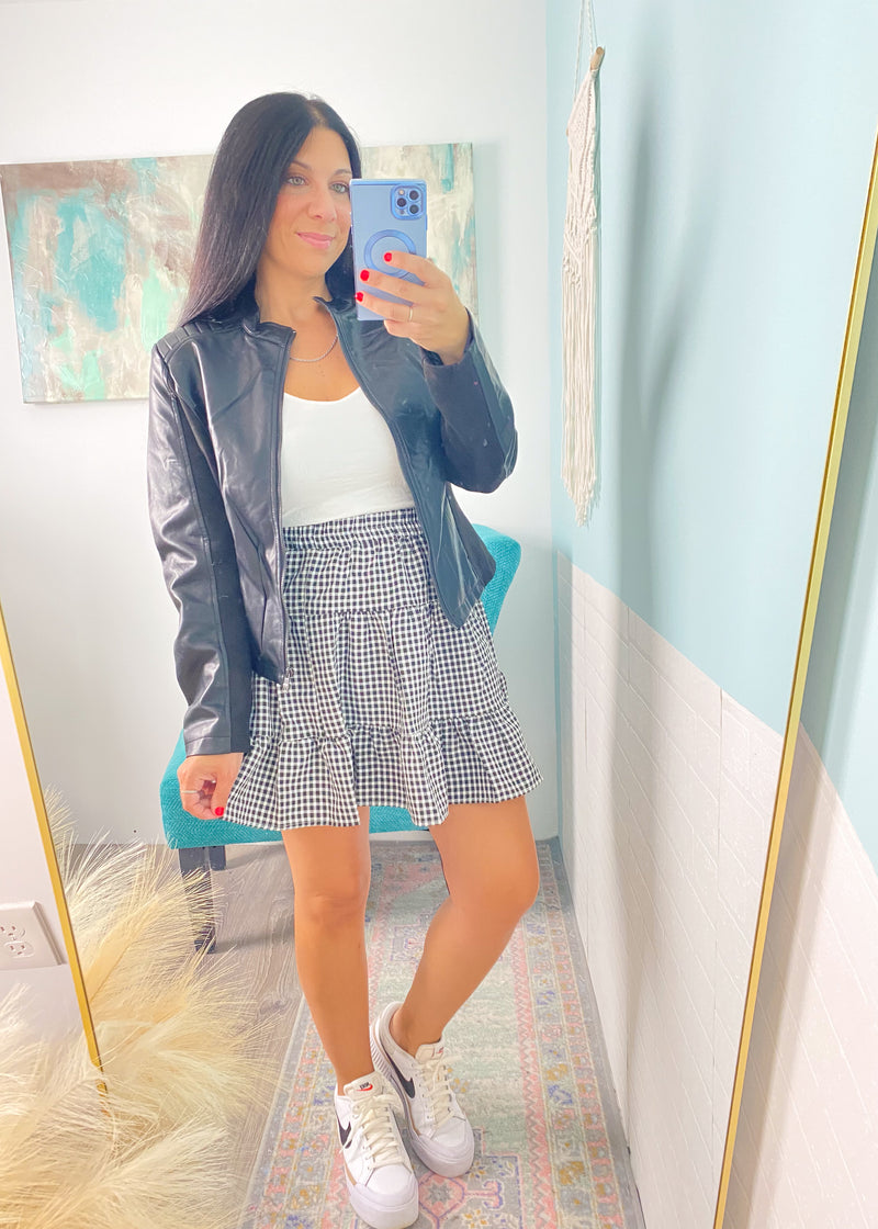 Woman taking a mirror selfie wearing a checkered skirt, white top, and sneakers in a room with colorful decor.