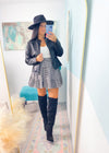 Woman taking a mirror selfie wearing a black leather jacket, white top, plaid skirt, and knee-high boots.