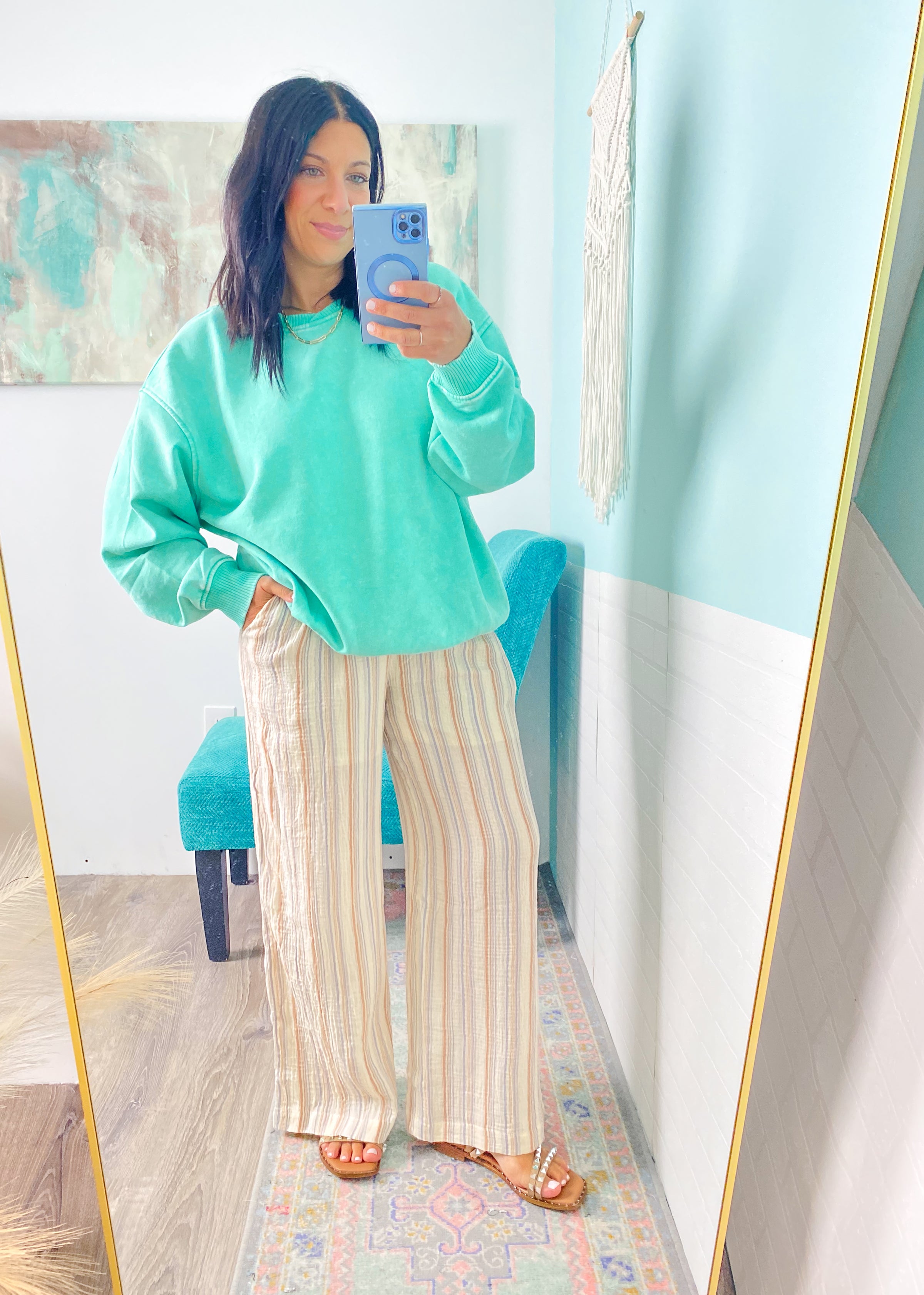 Person wearing a teal sweater and striped pants taking a mirror selfie.
