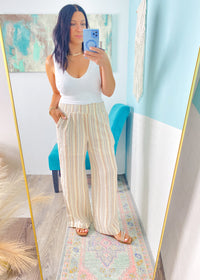 Woman taking a mirror selfie wearing a white top and striped pants in a room with colorful decor.