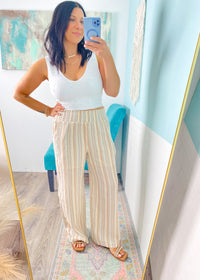 Woman taking a mirror selfie wearing a white top and striped pants in a room with a colorful rug and blue chair.