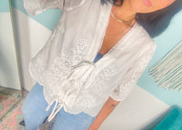 Person wearing a white lace top and blue jeans against a colorful wall.