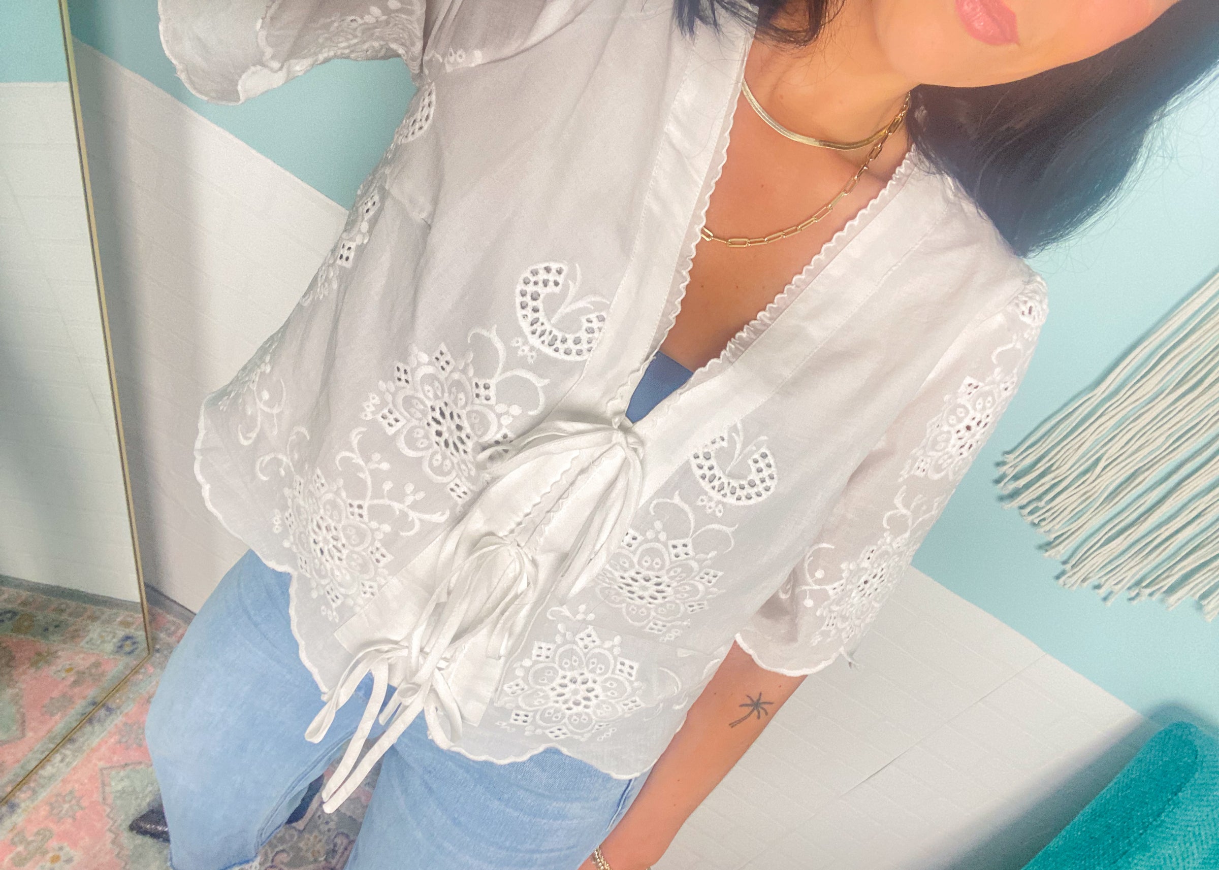 Person wearing a white lace top and blue jeans against a colorful wall.