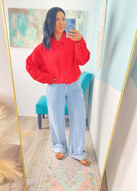 Woman wearing a red button up gauze shirt and blue jeans taking a mirror selfie.