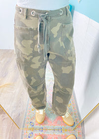 Camouflage pants on a mannequin with a colorful rug and light blue wall in the background