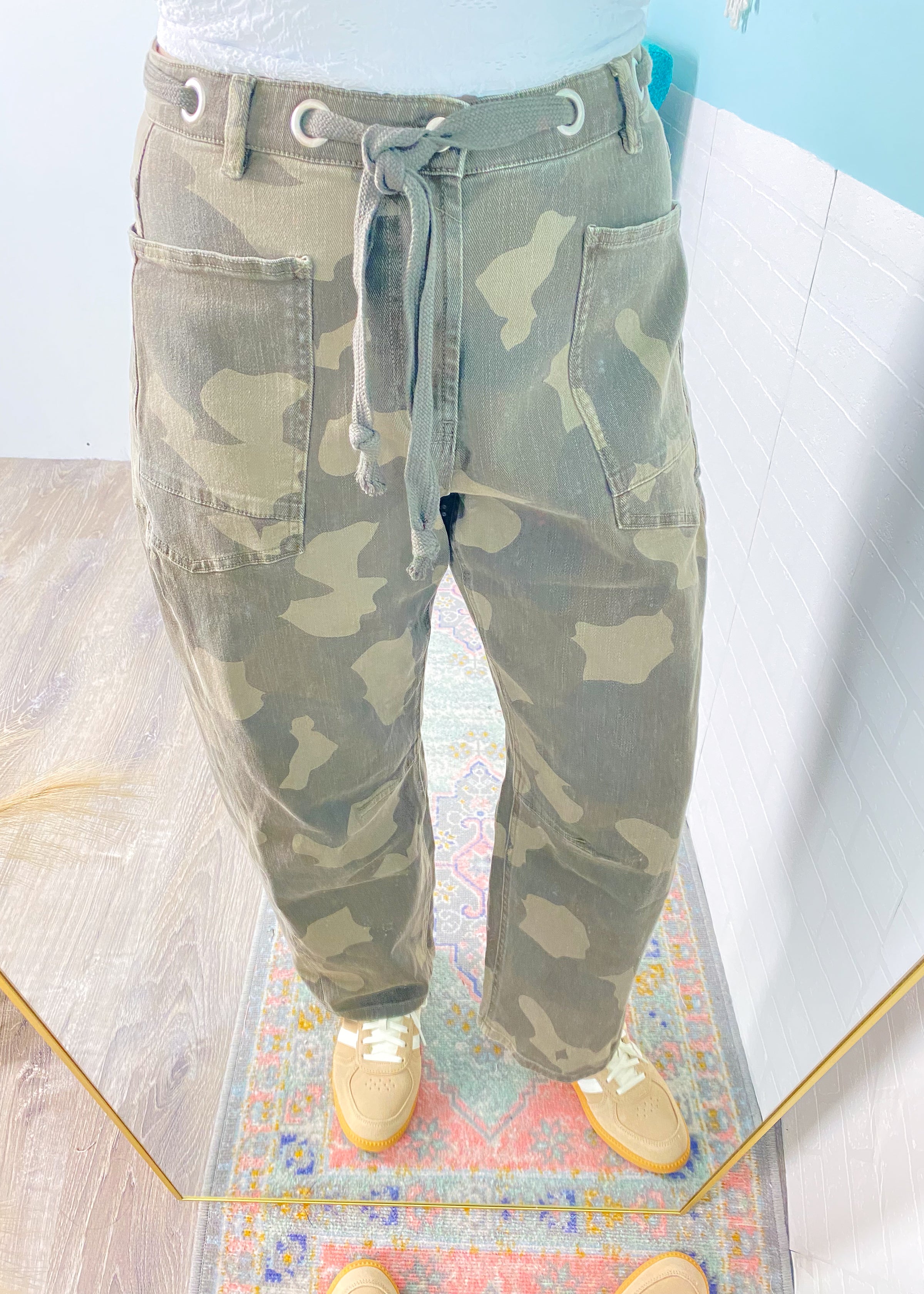 Camouflage pants on a mannequin with a colorful rug and light blue wall in the background